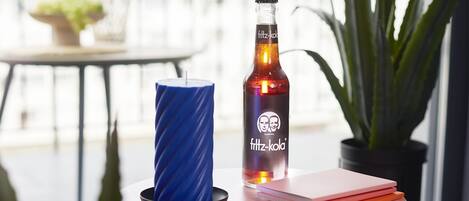 A pink table with a bottle of Fritz-Kola, a blue candle, and a notebook on it.