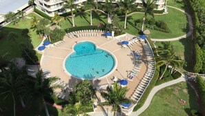 Vista aérea de un complejo turístico con una piscina central rodeada de zonas de descanso y palmeras.