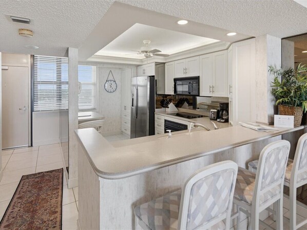 A modern kitchen with white cabinetry, stainless steel appliances, a central island with bar stools, and a ceiling fan.