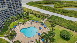 A hotel with a large pool surrounded by lounge chairs and umbrellas, a view of the ocean, and a mangrove area. - Beachfront 2BR/2BA South Seas condo with pool, WiFi, and beach access (Marco Island)