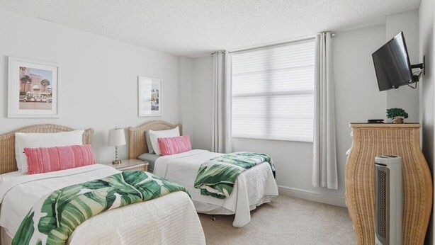 A hotel room with two beds, a flat-screen TV, a standing heater, and a window with curtains. - Beachfront 2BR/2BA South Seas condo with pool, WiFi, and beach access (Marco Island)