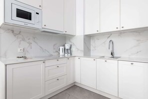 A modern kitchen with white cabinets, a built-in microwave, a coffee maker, and a sink.