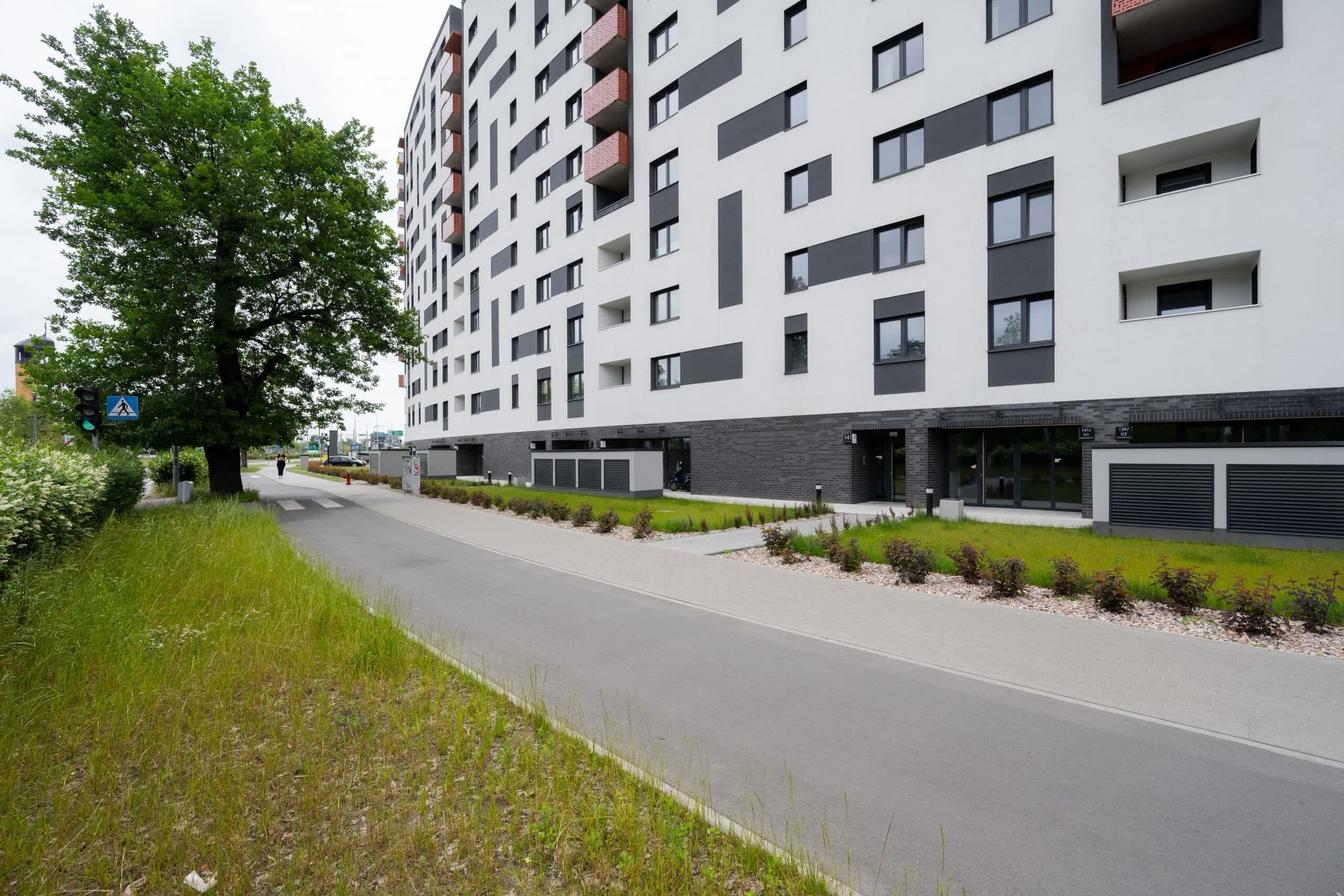 Un bâtiment moderne à plusieurs étages, doté d’une promenade piétonne, d’un grand arbre et surplombant un ciel dégagé.