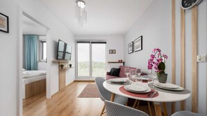 A modern living room with a dining area, a sofa, a TV, and a view through a glass door.