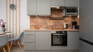 A modern kitchen with grey cabinets, a brick backsplash, a microwave, an oven, and a sink.