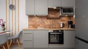Een moderne keuken met grijze kastjes, een tegelwand van baksteen, een magnetron, een oven en een spoelbak.