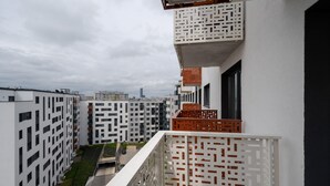 A modern apartment building with a geometric facade, balconies with patterned railings, and a view of the cityscape in the background.