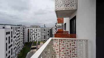 Un moderno edificio de apartamentos con fachada geométrica, balcones con barandillas ornamentadas y vistas de la ciudad al fondo.