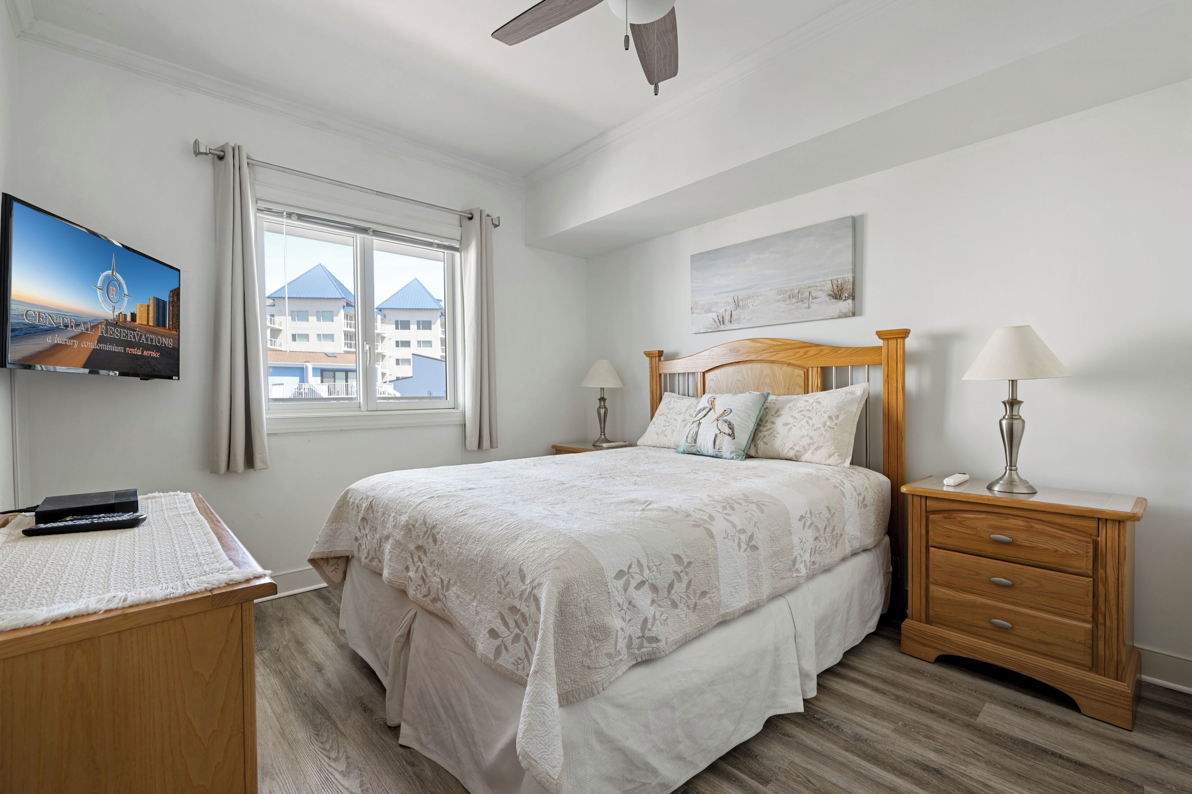 Une chambre à coucher avec un lit, des tables de chevet, un bureau, une télévision et une fenêtre avec des rideaux.