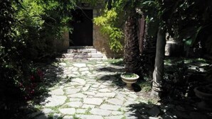 Un sendero de piedra que conduce a una puerta oscura rodeada de abundante vegetación y plantas en macetas.