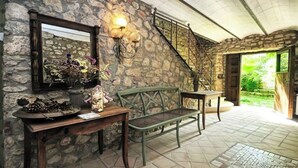 Una habitación con paredes de piedra, un banco de madera, una mesa con espejo y flores, y una escalera que lleva a un área exterior.