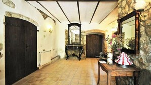 Un pasillo con paredes de piedra, suelo de baldosas y una mesa de madera con una lámpara y adornos.