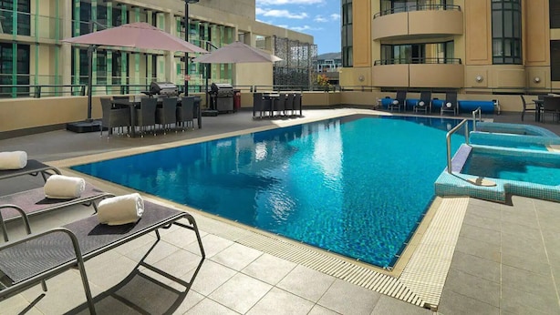 A rooftop pool area with lounge chairs and umbrellas, surrounded by modern buildings.