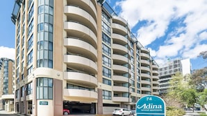 A multi-story building with a curved facade, a parking garage entrance, and a sign indicating 'Adina serviced apartments'.