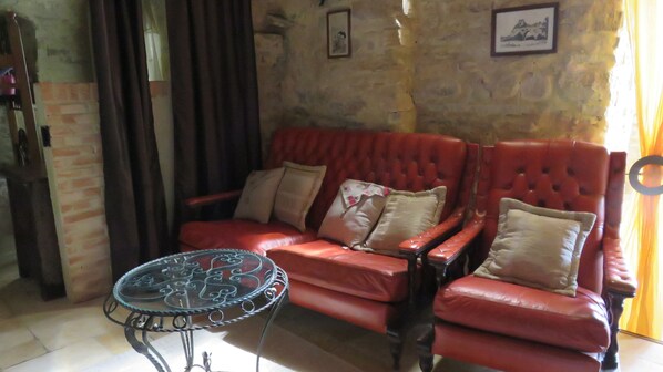 A red leather sofa with cushions, a glass coffee table with metal legs, and a stone wall with a framed picture. - depontet-fronzele oil mill: gite "le laurier (Lagorce)