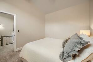 Une chambre à coucher avec un lit, une table de chevet, une lampe et une porte donnant sur un escalier.