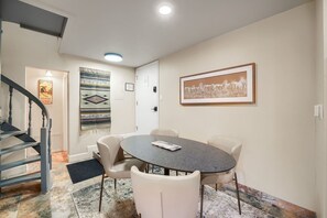 Un coin repas comprenant une table ronde, six chaises, un tapis et un tableau encadré accroché au mur.