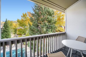 A balcony with a view of trees in autumn colors, a white table, and a wicker chair.