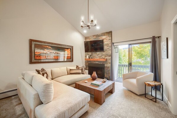 A living room with a sectional sofa, a coffee table, a fireplace, and a television mounted on a stone wall.