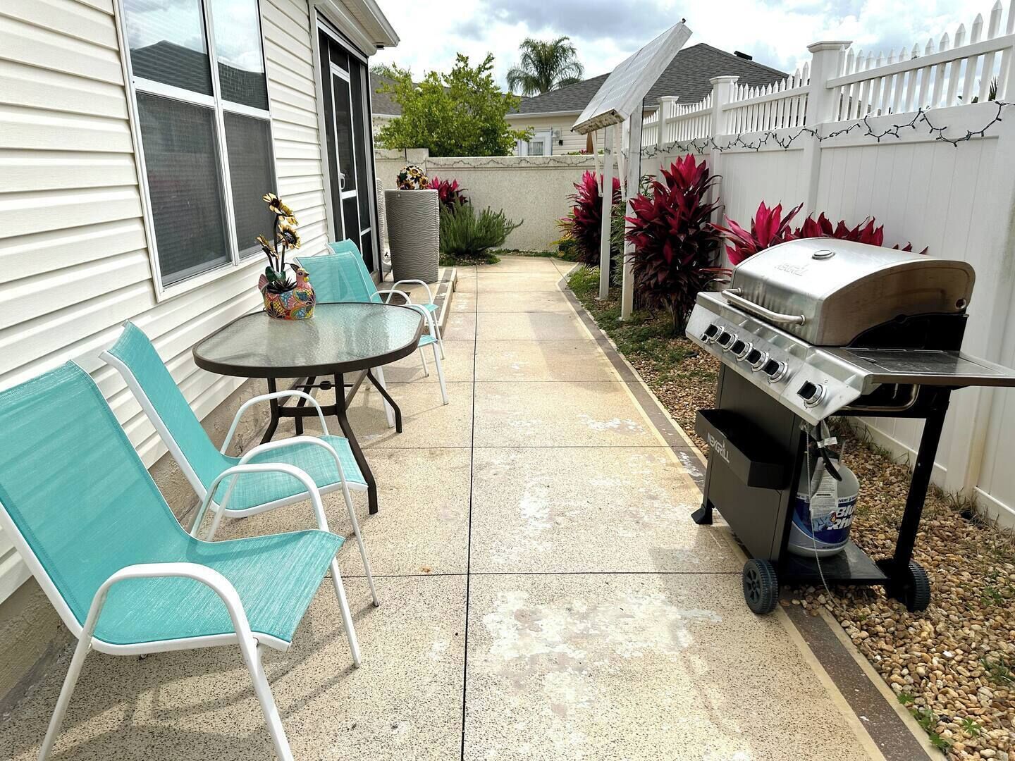 Eine Terrasse mit Grill, Sitzgelegenheiten im Freien und ein Haus mit weißem Zaun.