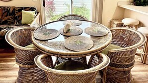 A dining area with a round table surrounded by wicker chairs, a hanging light fixture, and a view through a glass door to the outside. - Sun Splashed - 3/2 w/ Golf Cart in The Village of Amelia (The Villages)