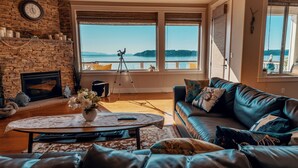 A living room with a fireplace, a large window with a view of the water, a sofa, and a coffee table. - Stunning House with Views of Puget Sound Ideal for Family Reunions (Edmonds)