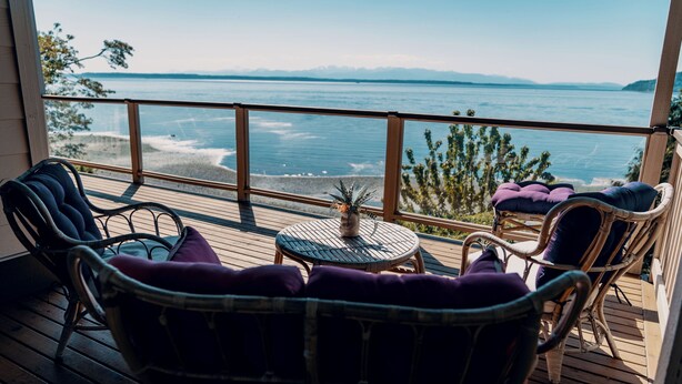 A wooden deck with wicker chairs and a small table, overlooking a beach and ocean. - Stunning House with Views of Puget Sound Ideal for Family Reunions (Edmonds)
