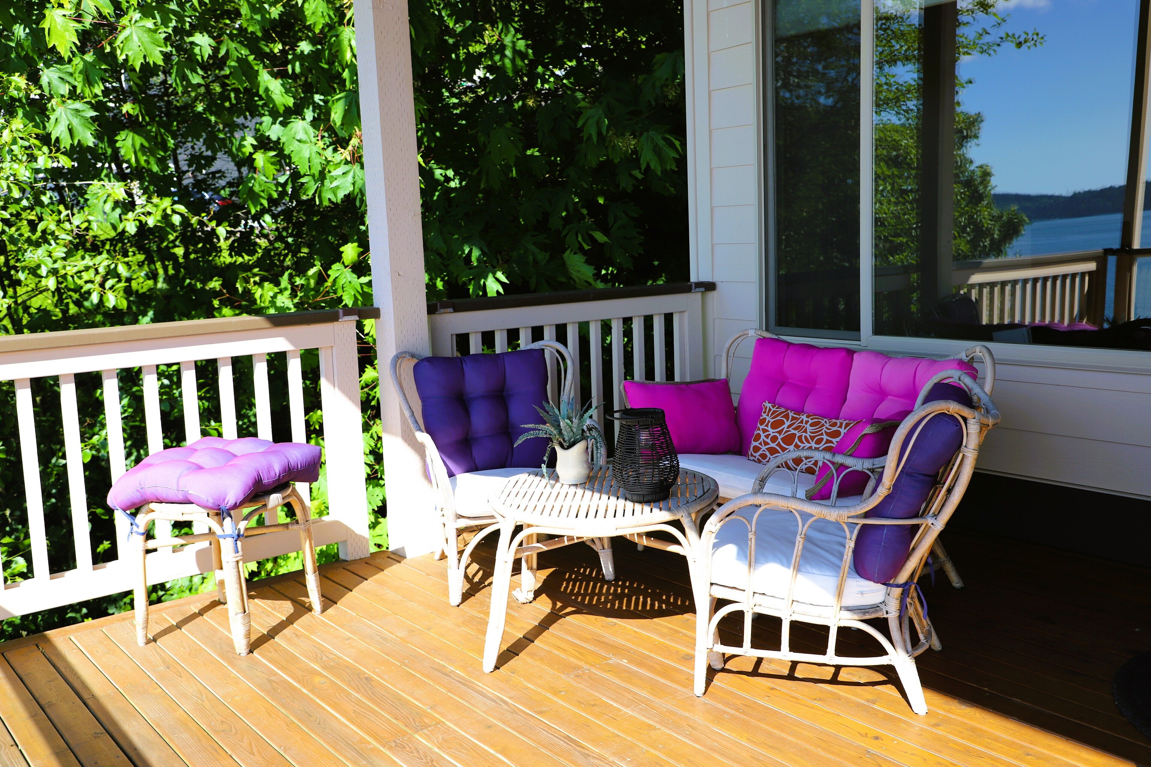 A wooden deck with wicker furniture, including a chair and a sofa with cushions.
