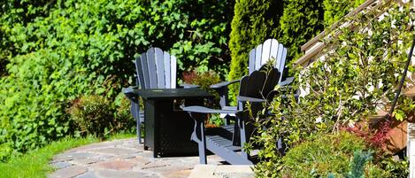 Une terrasse aménagée dans un jardin, avec des fauteuils Adirondack, un chemin de pierres et une végétation luxuriante.