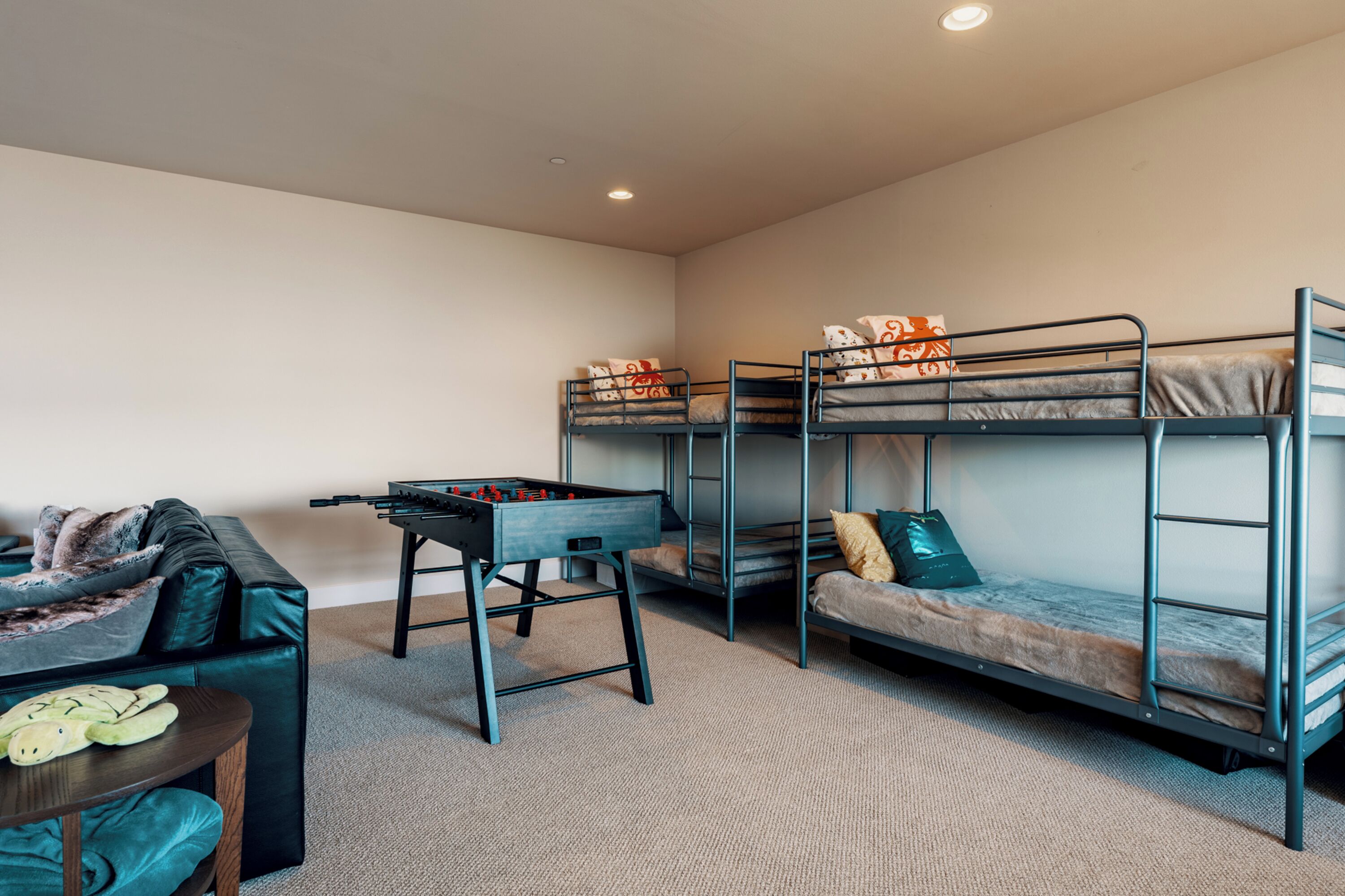 A room with bunk beds, a foosball table, a sofa, and a small table with slippers.