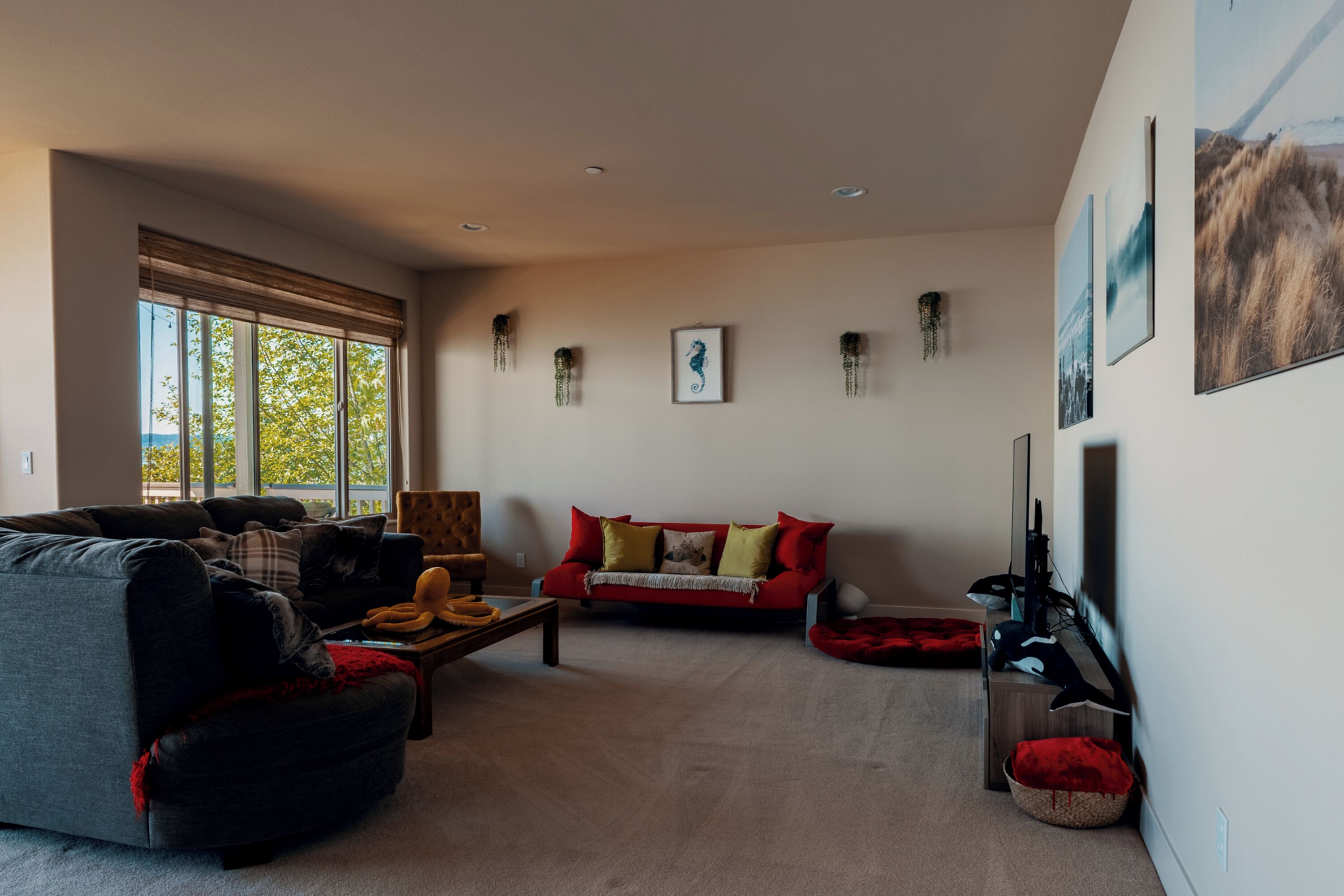 A spacious living room with a grey sofa, a red sofa, and a coffee table. There are wall-mounted decorations and a large window providing natural light.