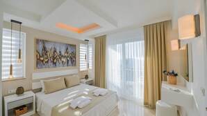 Una habitación de hotel moderna con una cama grande, una mesita de noche, un escritorio y un amplio ventanal con cortinas.
