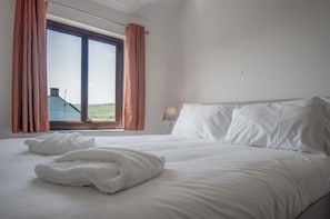 Quarto com uma cama grande, janela com cortinas e vista para um edifício.