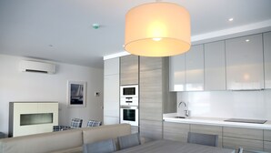 A modern kitchen with built-in appliances, a dining area with a table and chairs, and a large pendant light. - Apartamentos Turísticos da Nazaré (Nazaré)