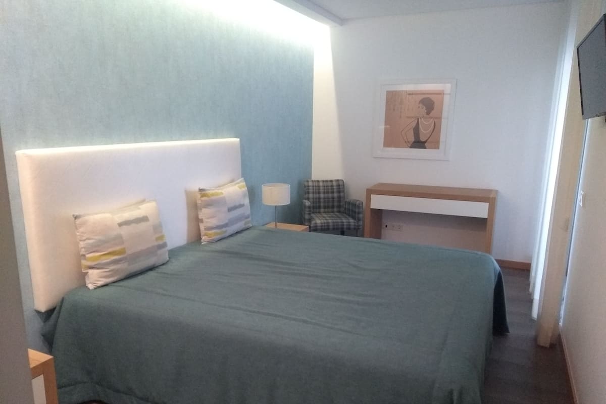 A bedroom with a bed, a chair, a desk, and a wall-mounted picture.