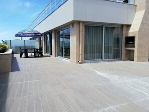 A modern outdoor patio with a table and chairs, a blue umbrella, and a glass-enclosed area with a grill. - Apartamentos Turísticos da Nazaré (Nazaré)