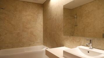 Un baño moderno con baldosas color beige, una bañera blanca y un lavamanos con un espejo encima.