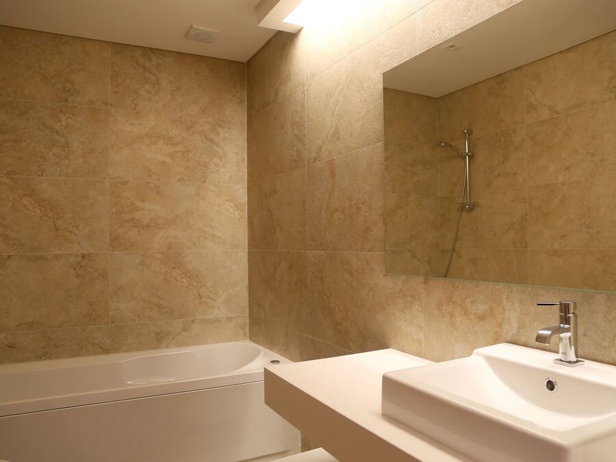 Ein modernes Badezimmer mit beige farbenen Fliesen, einer weißen Badewanne und einem Waschbecken mit Spiegel.
