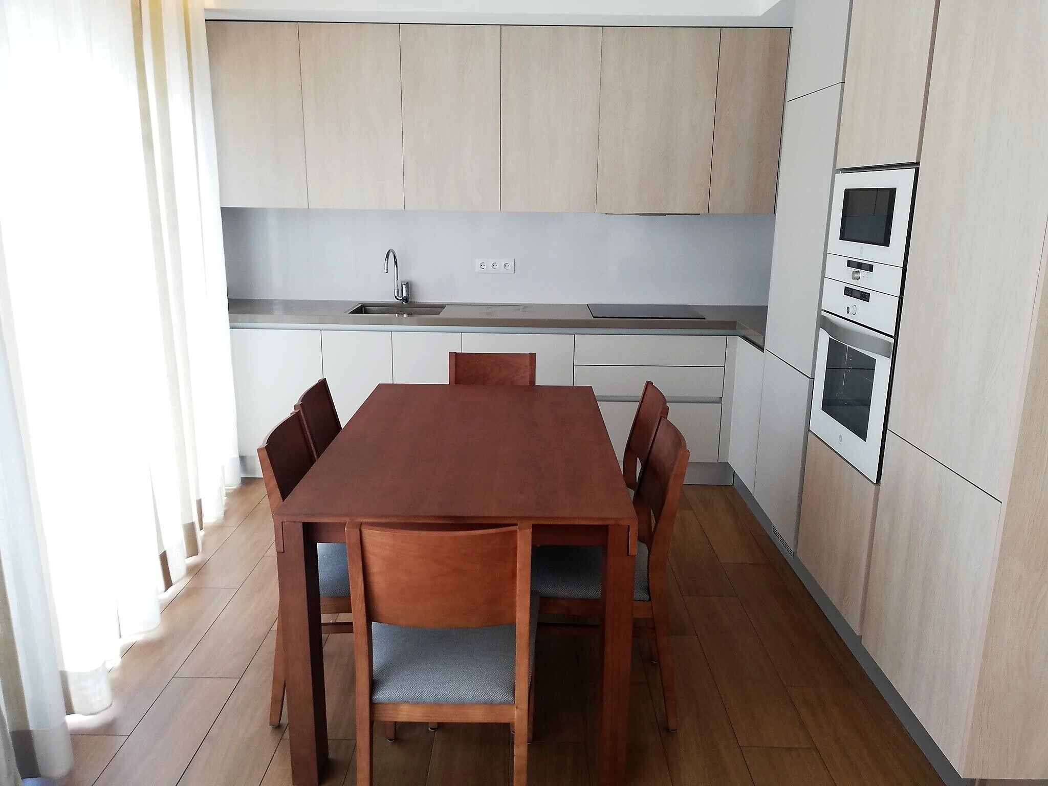 A modern kitchen with wooden cabinets, a built-in oven, and a dining table with chairs.