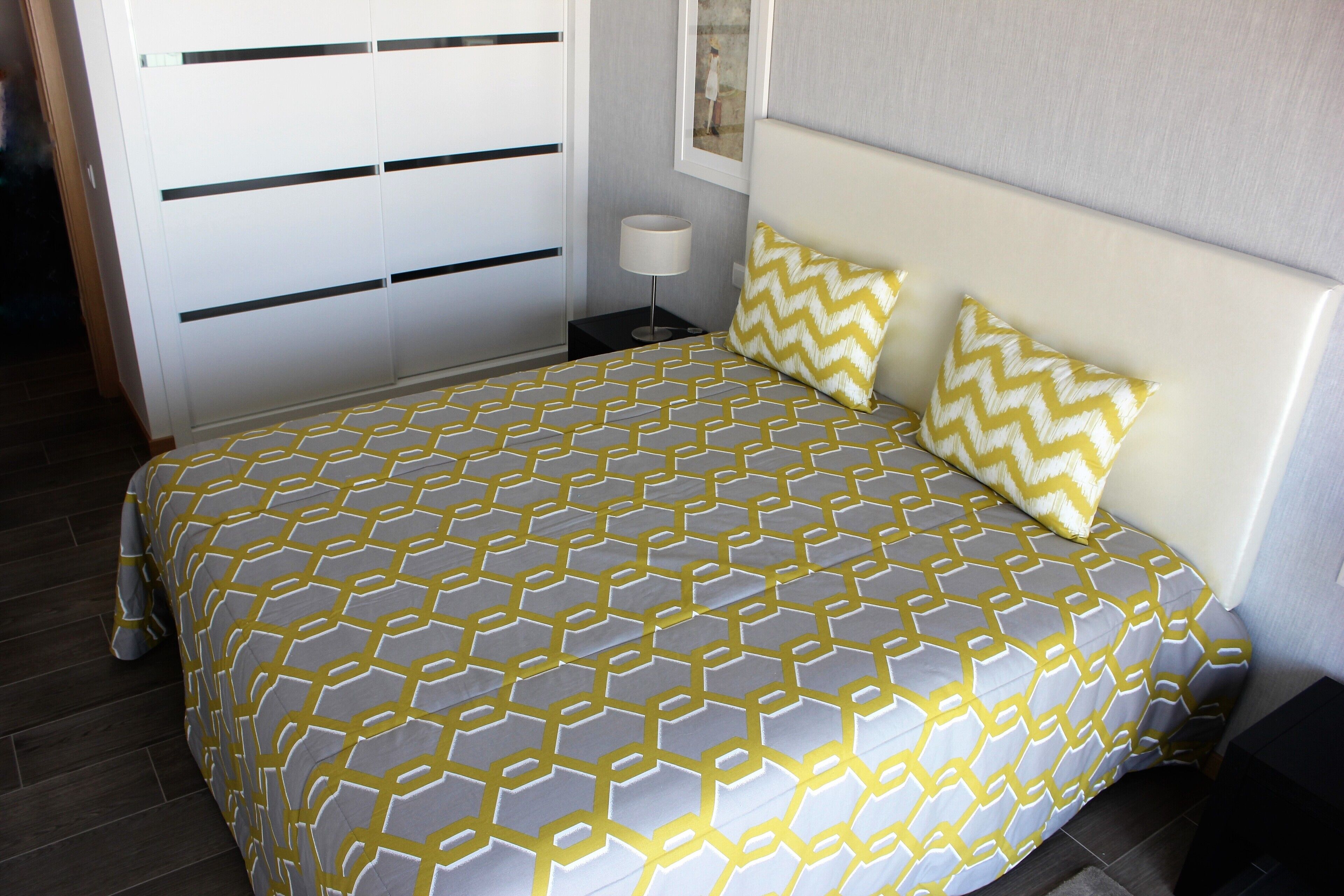 A neatly made bed with a geometric patterned bedspread, a white headboard, and two decorative pillows.