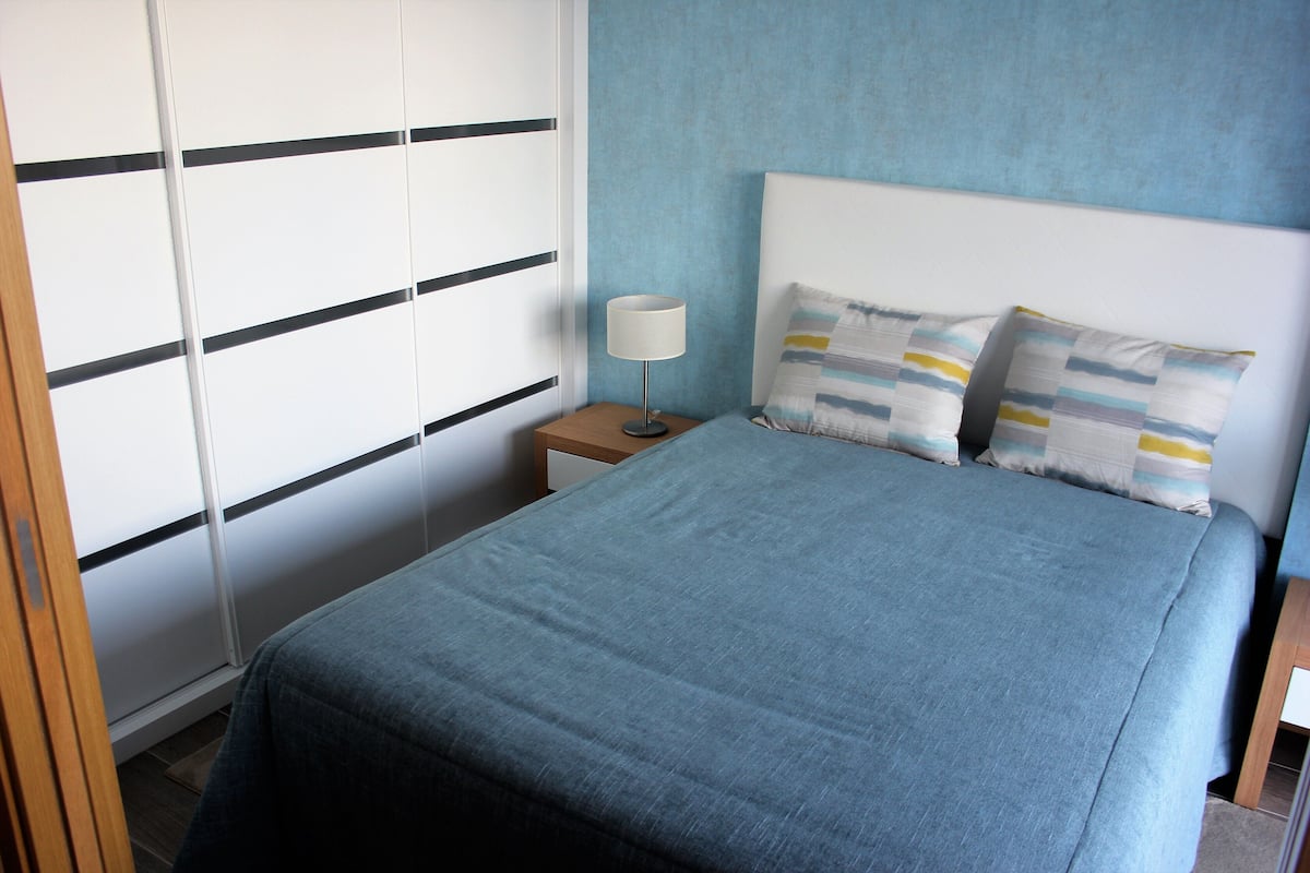 A bedroom with a bed, a nightstand, a lamp, and a wardrobe with sliding doors.