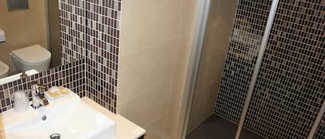 Et badeværelse med en hvid vask, toilet og brusekabine i glas.
