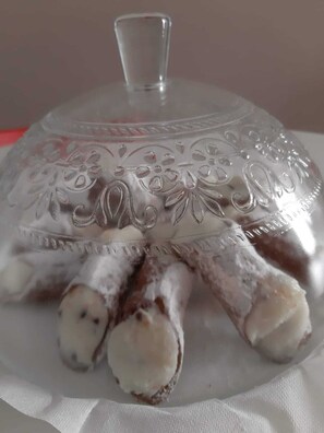 Una cúpula de vidrio transparente con diseños florales en relieve y un asa, cubriendo una bandeja con varios objetos blancos y marrones.