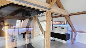 A modern loft bedroom with a glass wall, wooden beams, and a built-in desk.