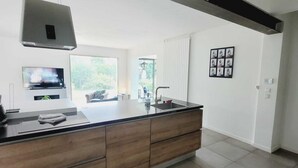 A modern kitchen with a large island, a built-in oven, and a window overlooking a garden.