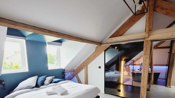 A bedroom with a large bed, a skylight, and a view of a balcony.