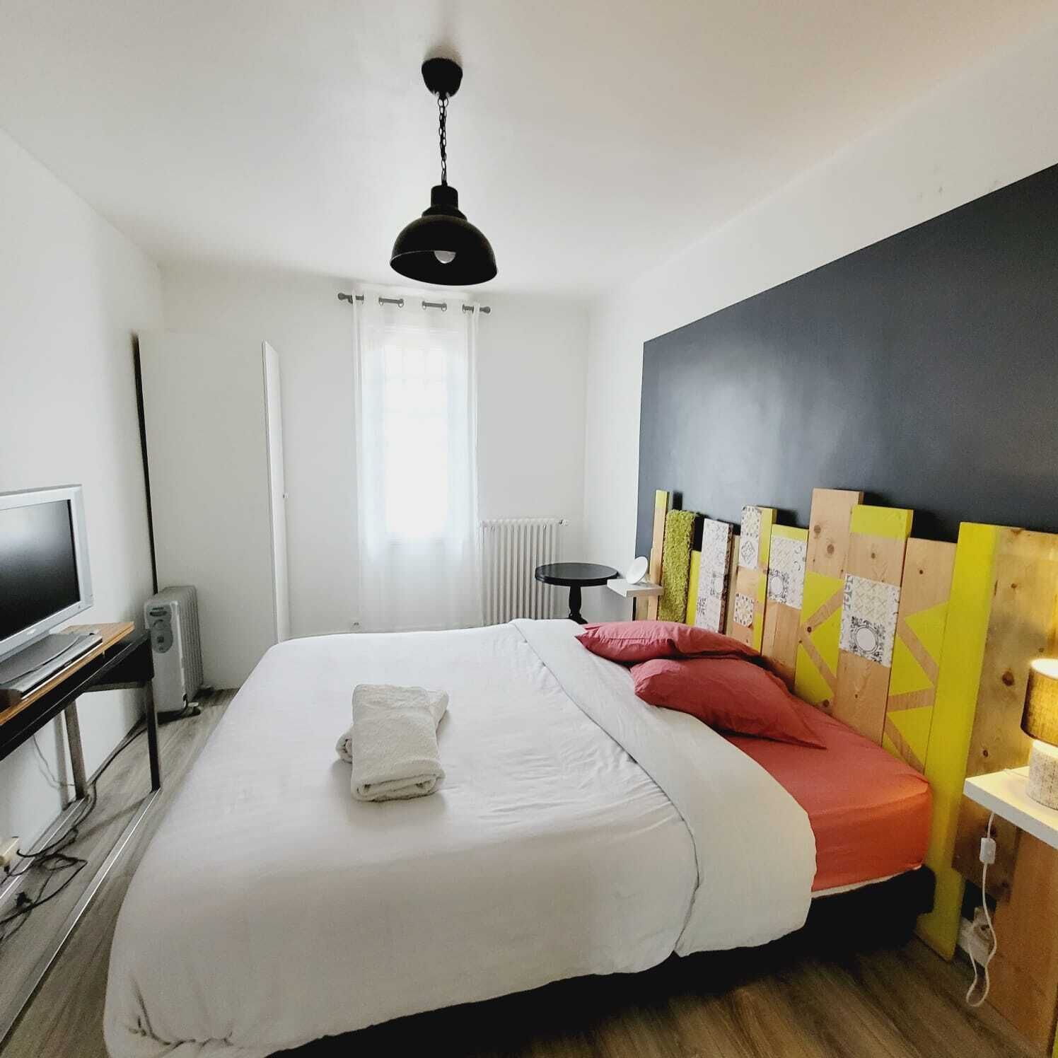 A hotel room with a bed, a desk with a computer, a radiator, and a window with curtains.