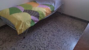 A small, single-bed room with a colorful quilt, a window, and a plain floor.