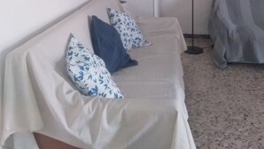 A room with a sofa, a lamp, a bed, and a wall-mounted artwork.