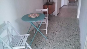 A small room with a white chair, a small table with a bowl of fruit, and a wooden cabinet.